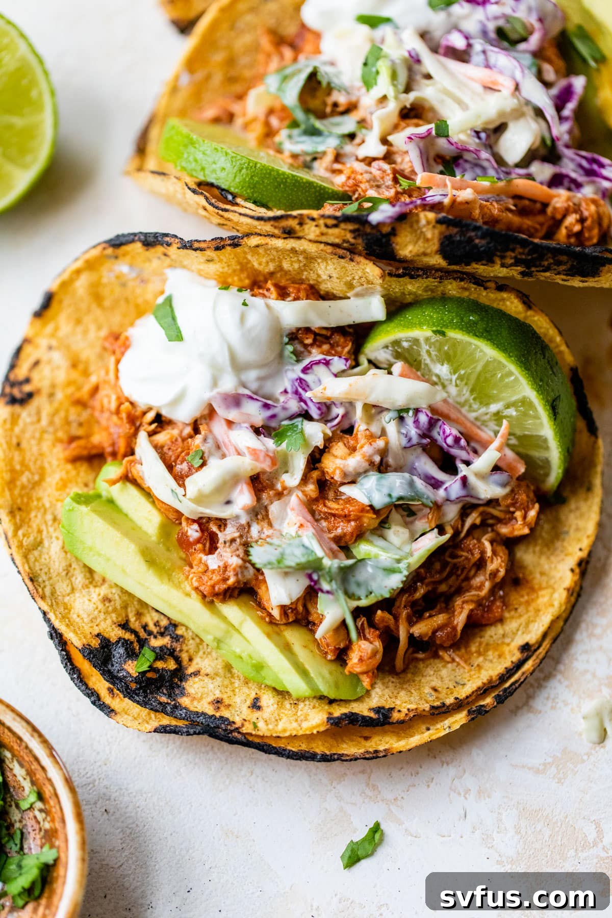 Delicious rotisserie chicken tacos topped with slaw, avocado, and a lime wedge, ready to be enjoyed