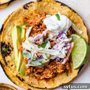 corn tortillas topped with shredded chicken, slaw, avocado, and a lime wedge