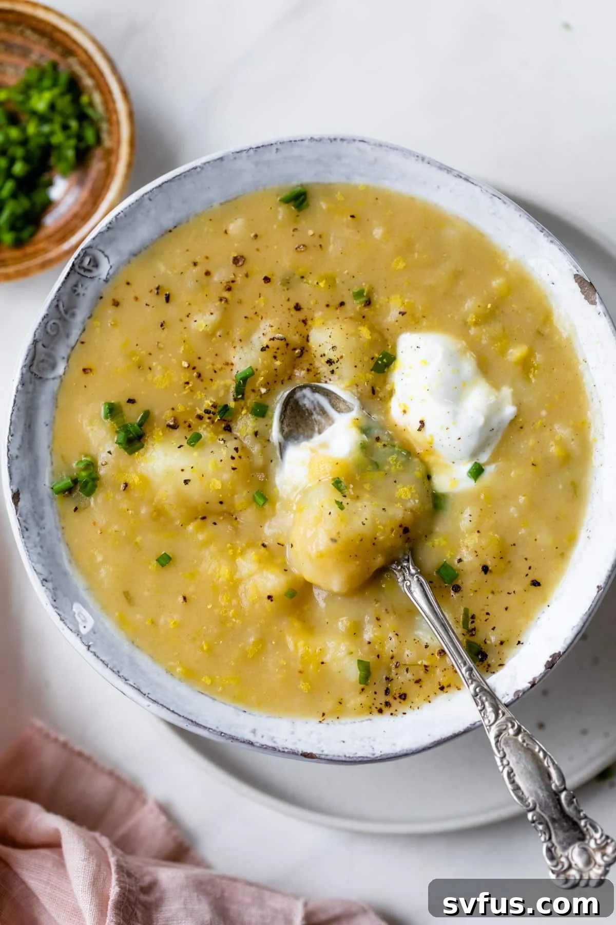 A beautifully presented bowl of creamy vegan potato leek soup, garnished with fresh herbs and a spoon resting in it, ready to be enjoyed.