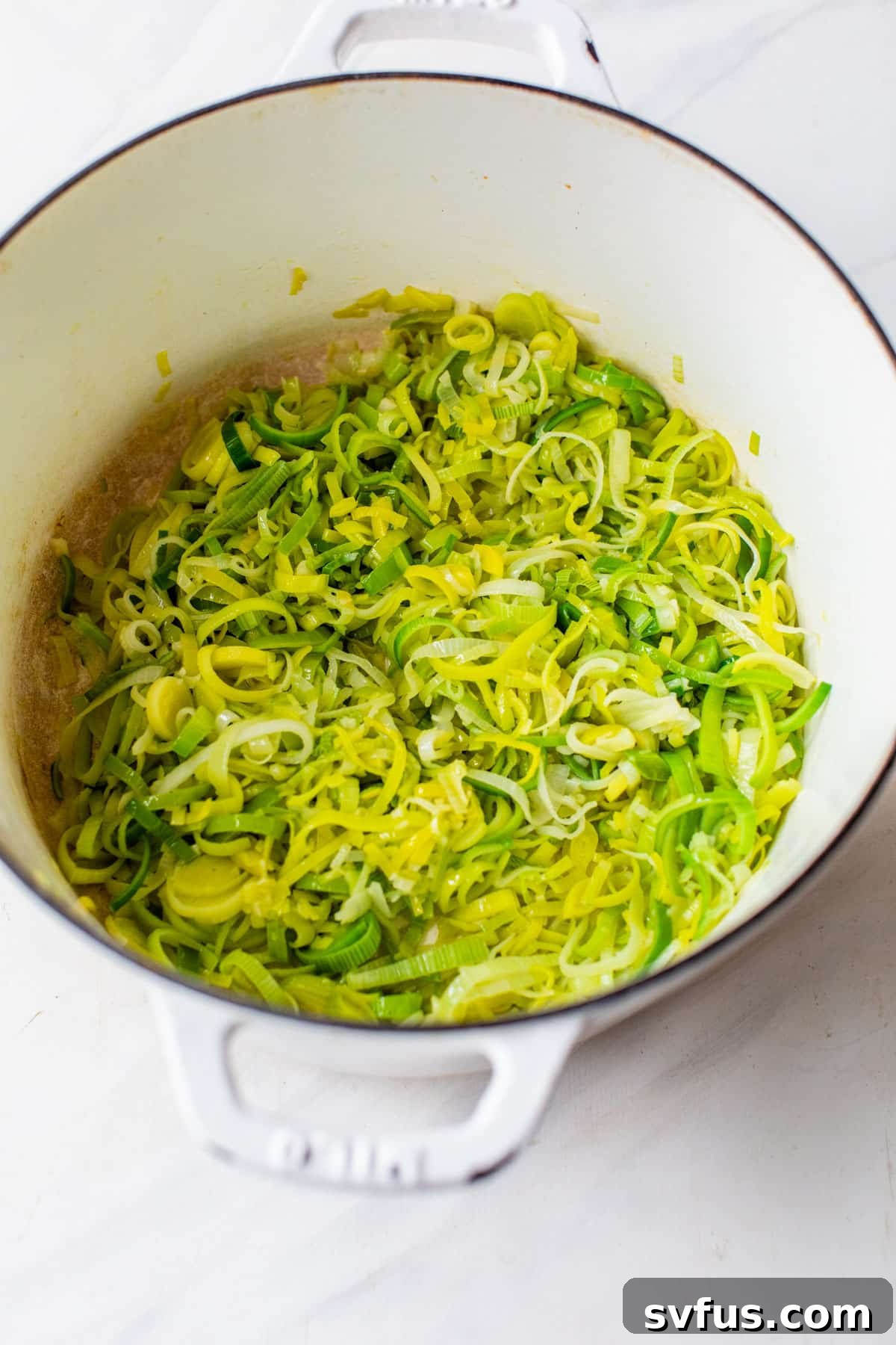 Freshly cleaned leeks cooking gently in vegan butter in a Dutch oven, softening to release their sweet aroma.