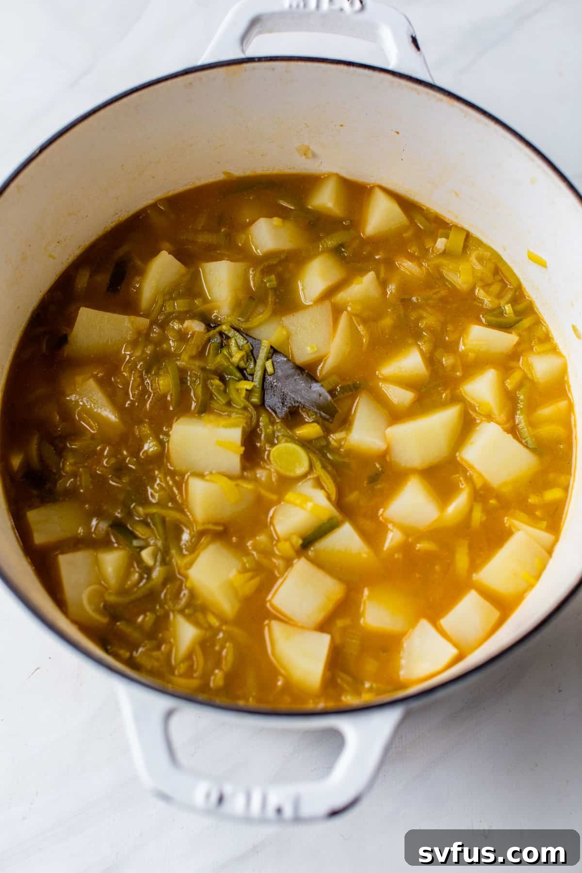 Diced potatoes, leeks, and vegetable broth simmering together in a Dutch oven, infusing with flavor.