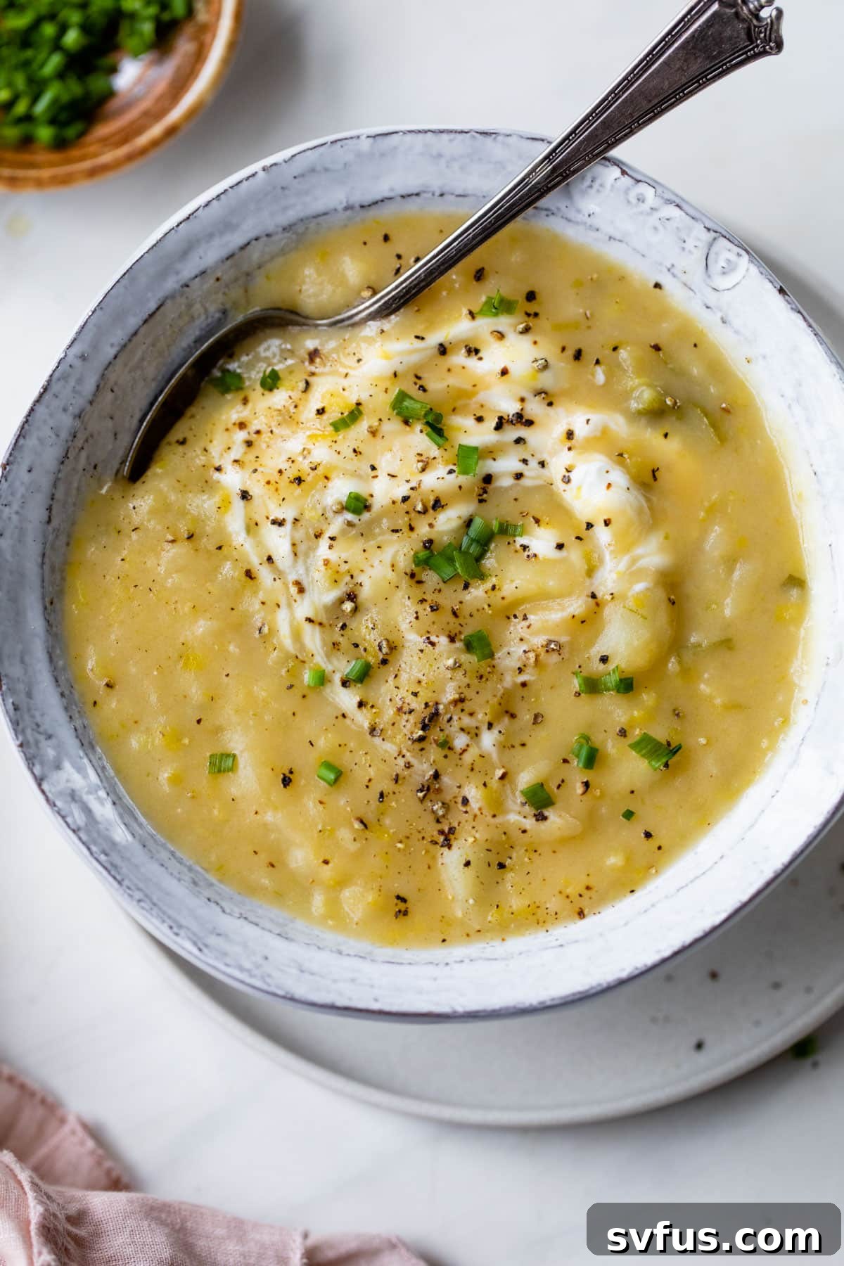 A comforting bowl of vegan potato leek soup, garnished and ready for serving, with a spoon nestled within.