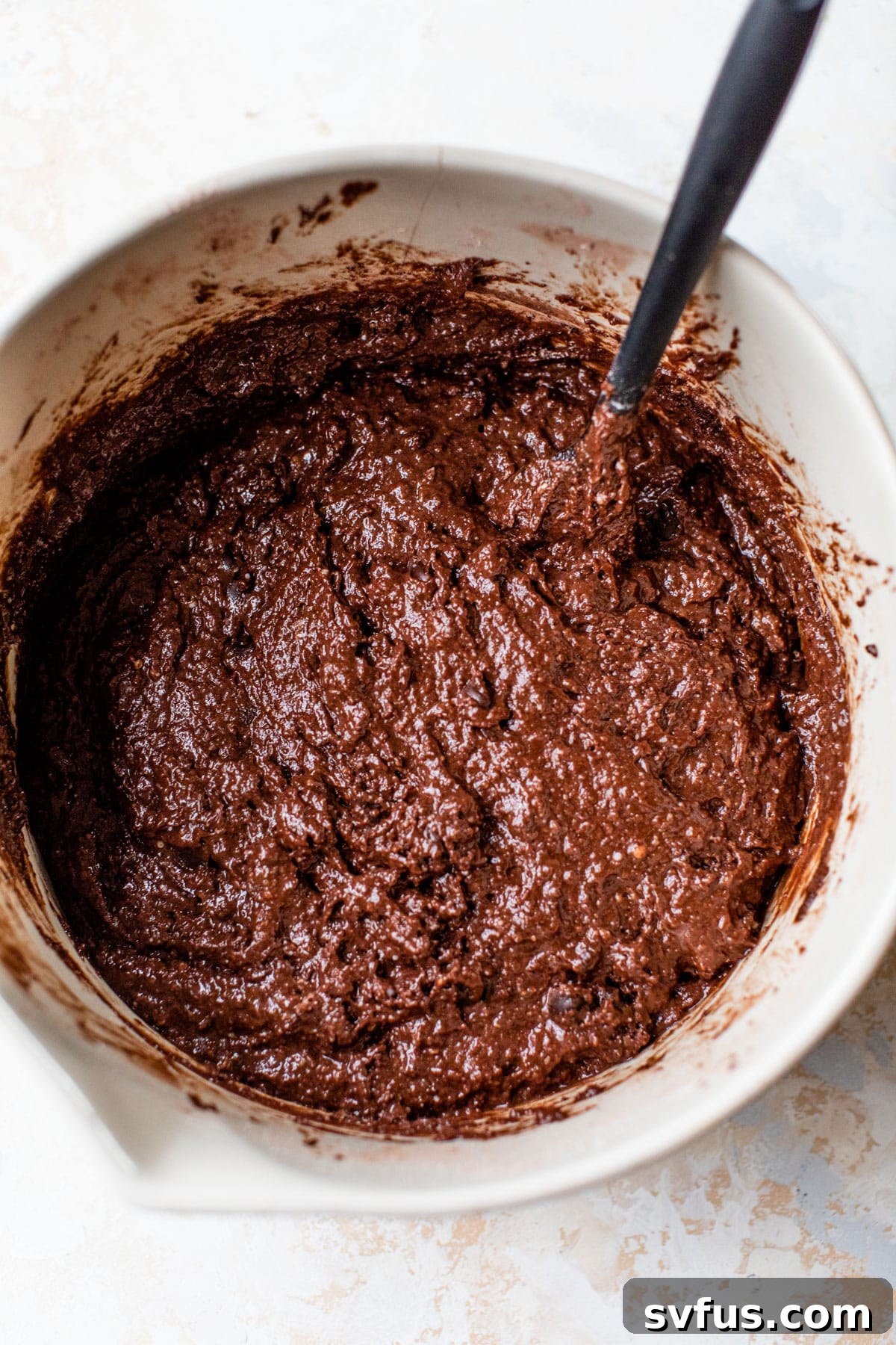 A mixing bowl filled with rich, dark vegan chocolate muffin batter, studded with chocolate chips, ready for baking.