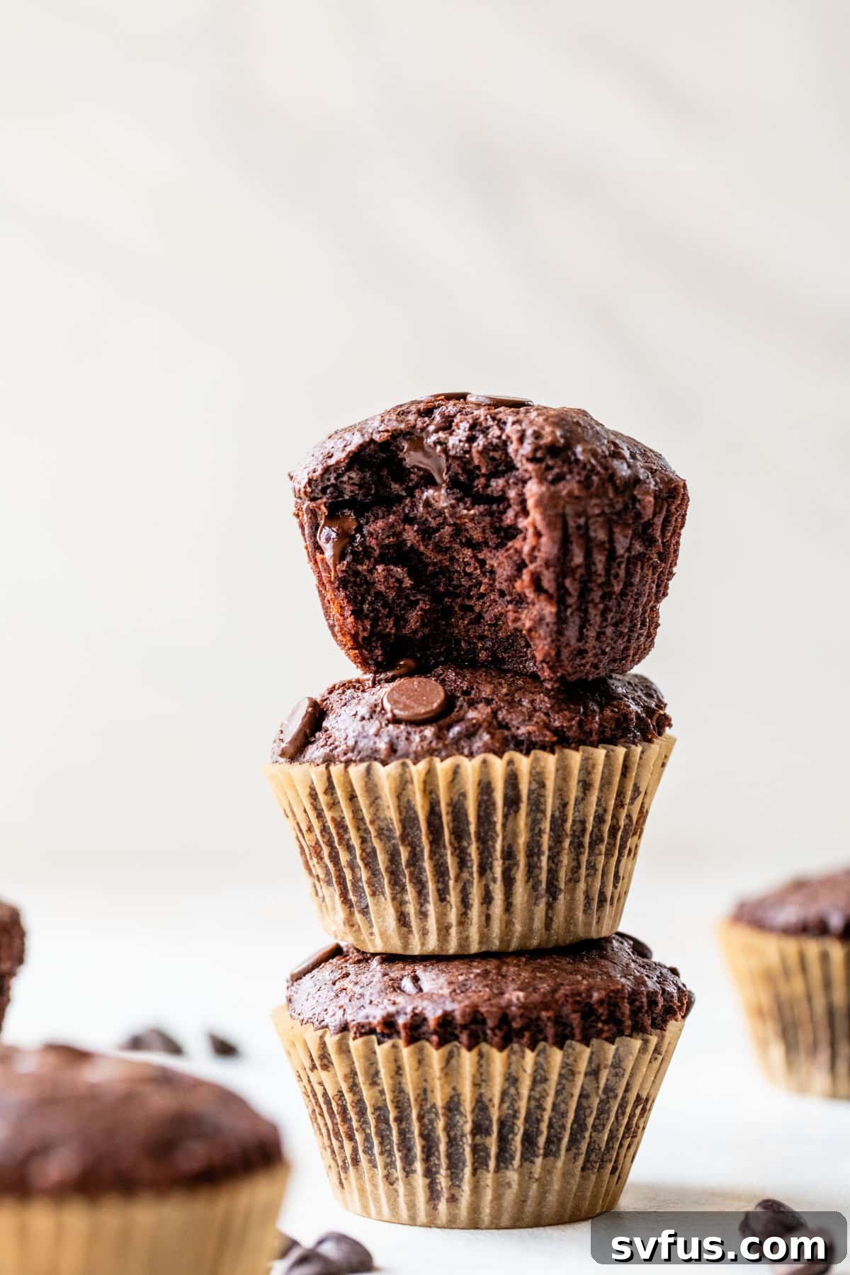 Three freshly baked vegan chocolate muffins stacked enticingly on top of each other, showcasing their perfectly domed tops and chocolate chips.