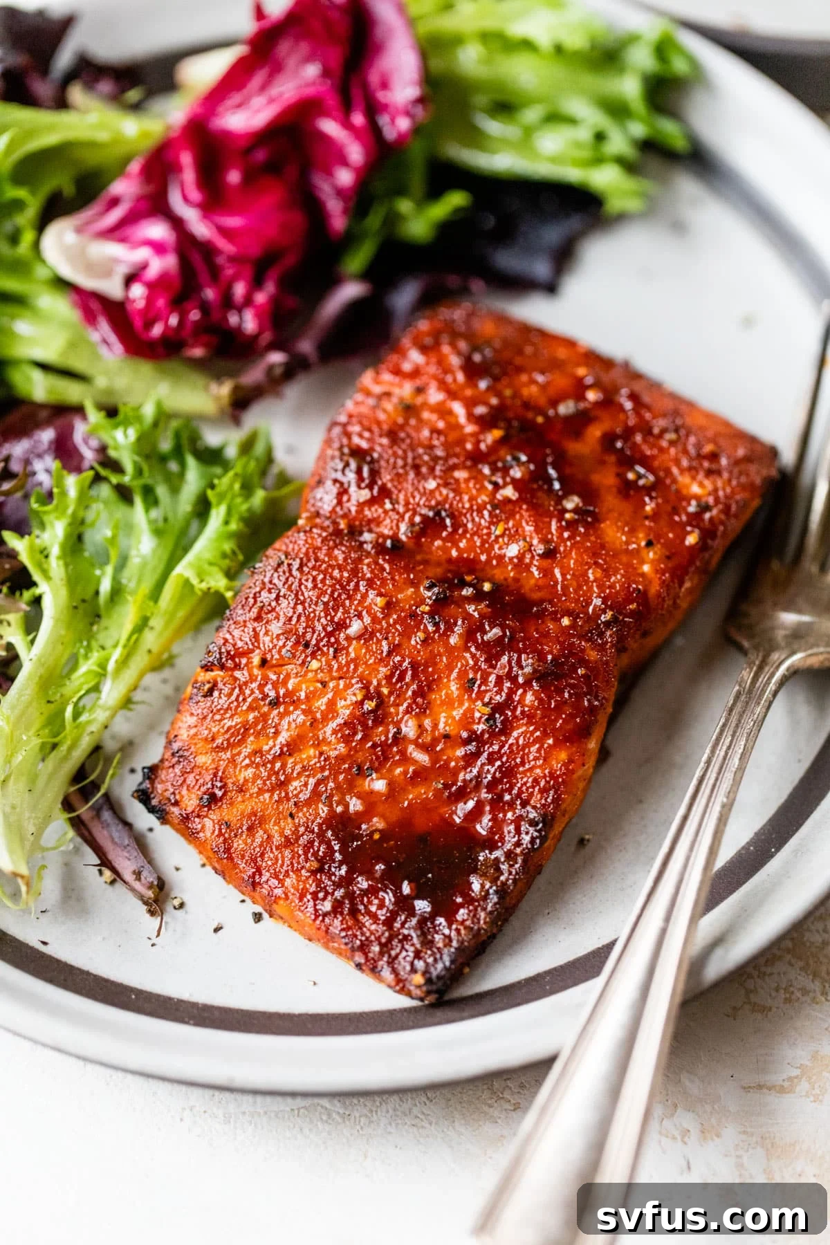 A perfectly cooked, flaky salmon fillet resting on a bed of fresh lettuce, accompanied by a fork, showcasing its golden-brown exterior and moist interior.
