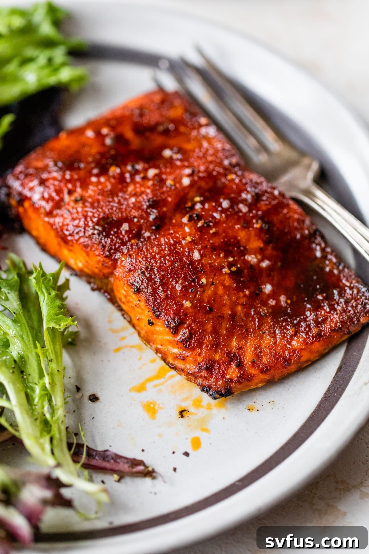A close-up image of a cooked salmon fillet on a white plate, garnished with fresh greens and a fork, highlighting its succulent texture and golden sear.