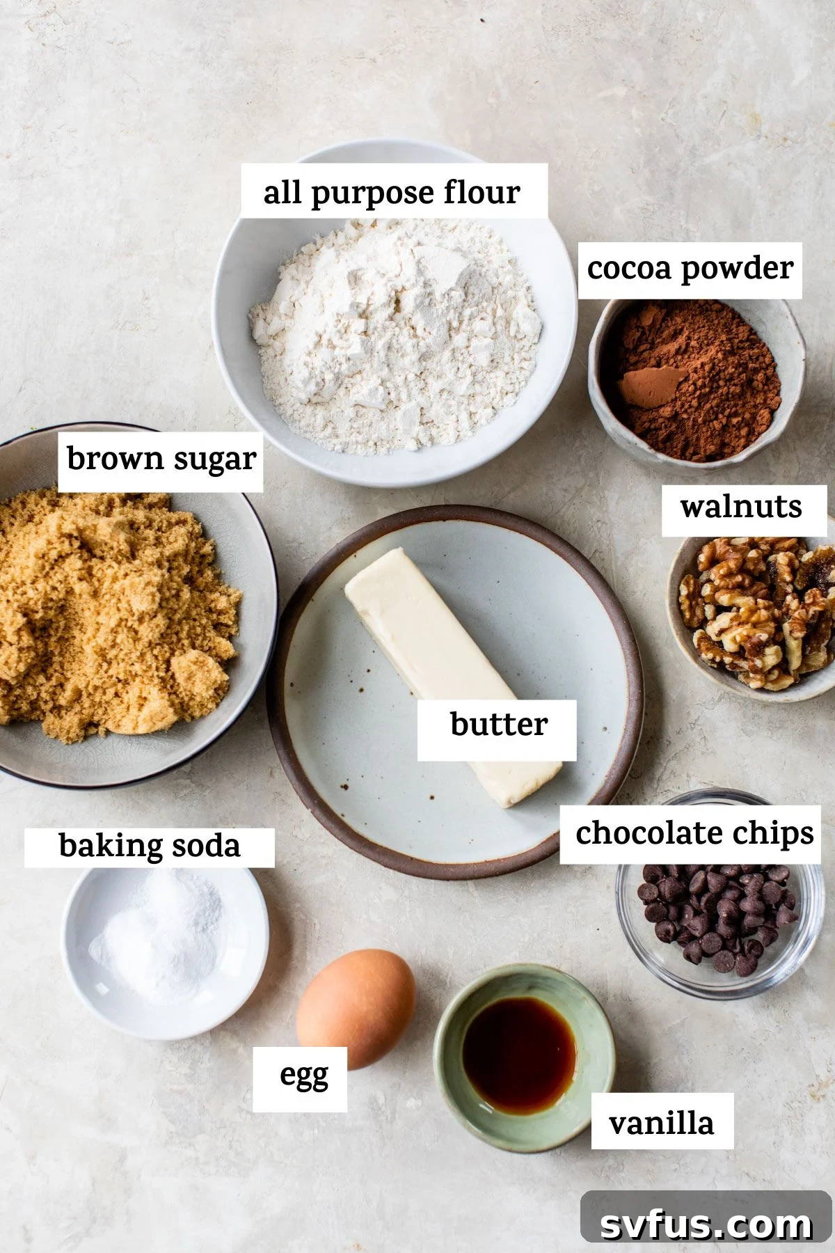 A collection of essential baking ingredients laid out on a clean white surface, including bags of flour and brown sugar, a stick of butter, eggs, vanilla extract, and a bowl of chocolate chips, all ready for baking delicious cookies.