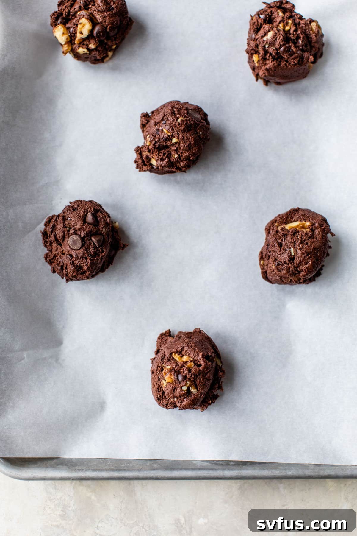 Raw, perfectly scooped double chocolate walnut cookie dough balls arranged neatly on a parchment-lined baking sheet, evenly spaced and ready to be placed into the oven for baking.
