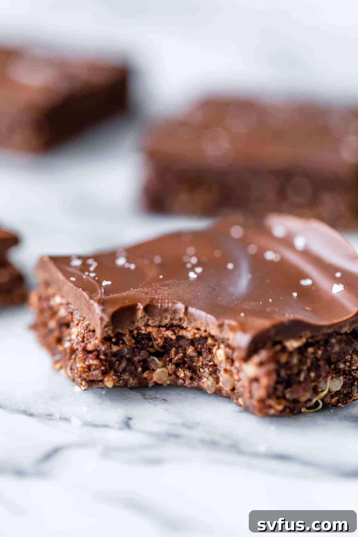 A single chocolate quinoa bar with a bite taken out, showing its rich, chewy interior and smooth chocolate topping.