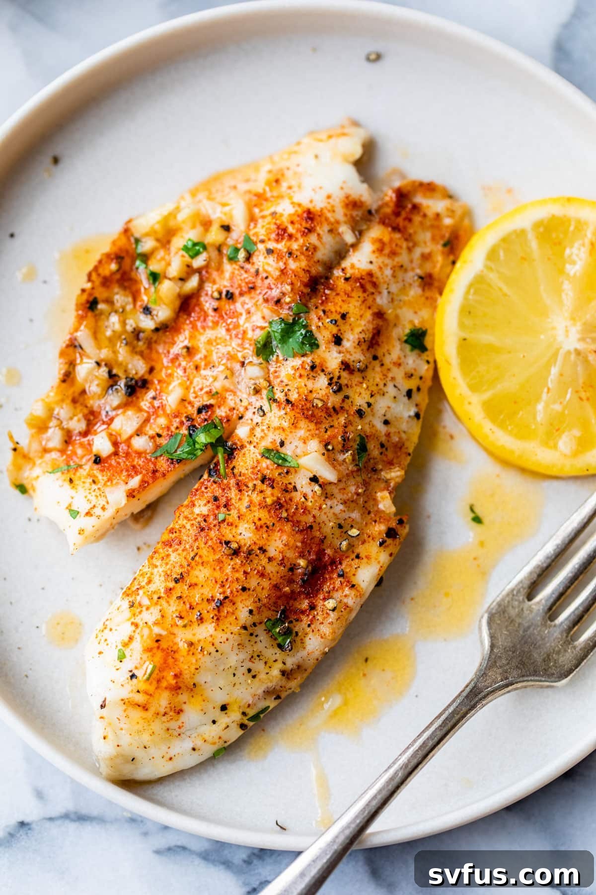Perfectly baked tilapia served on a plate with a fork, garnished with fresh herbs and lemon slices