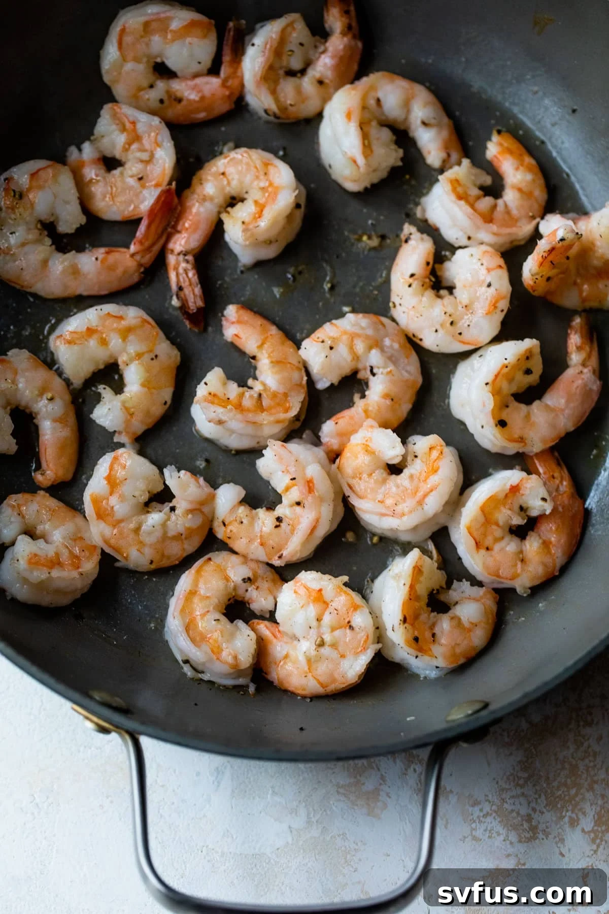 Shrimp perfectly searing in a hot skillet, turning pink and ready to be removed.