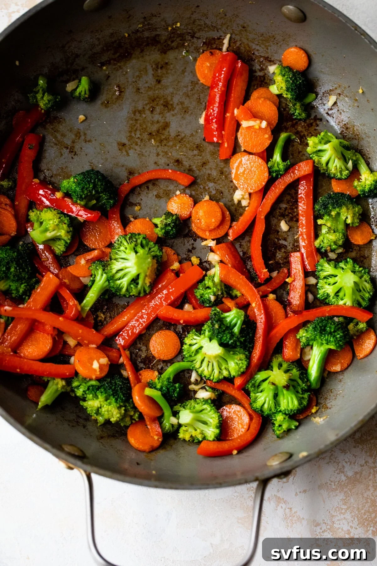 A colorful medley of broccoli, carrots, and bell pepper sizzling in a skillet.