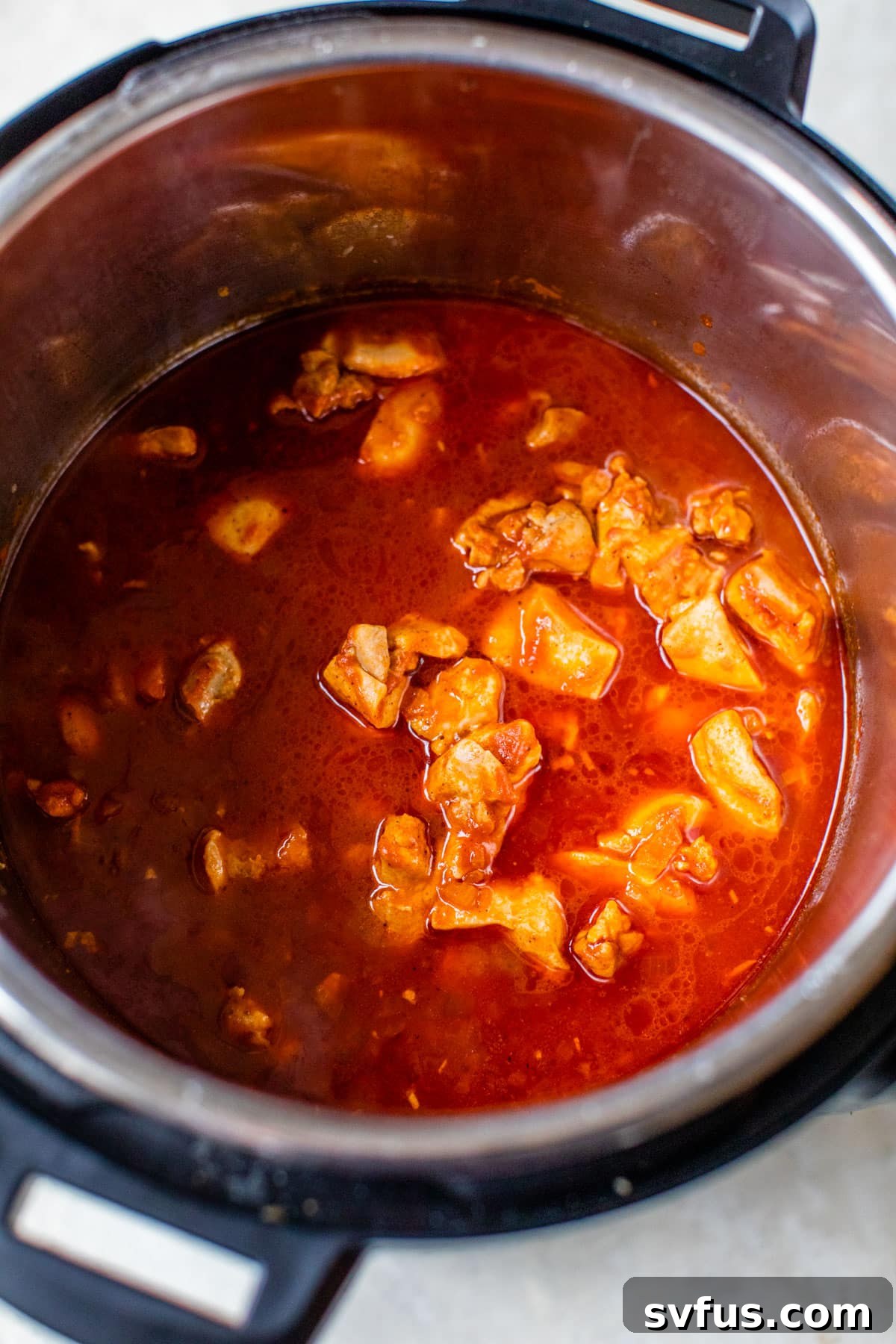 An Instant Pot filled with diced chicken, tomato sauce, and water, ready for pressure cooking.