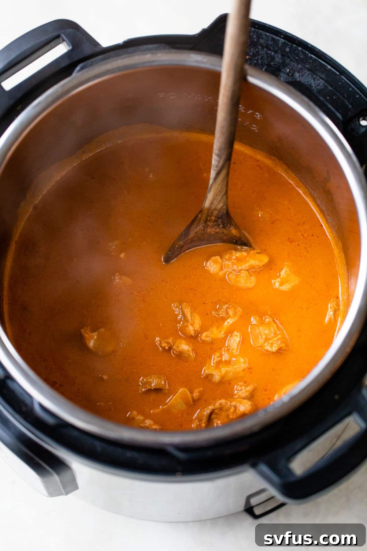 The finished Instant Pot Butter Chicken simmering in the pot, with a wooden spoon stirring the creamy sauce.