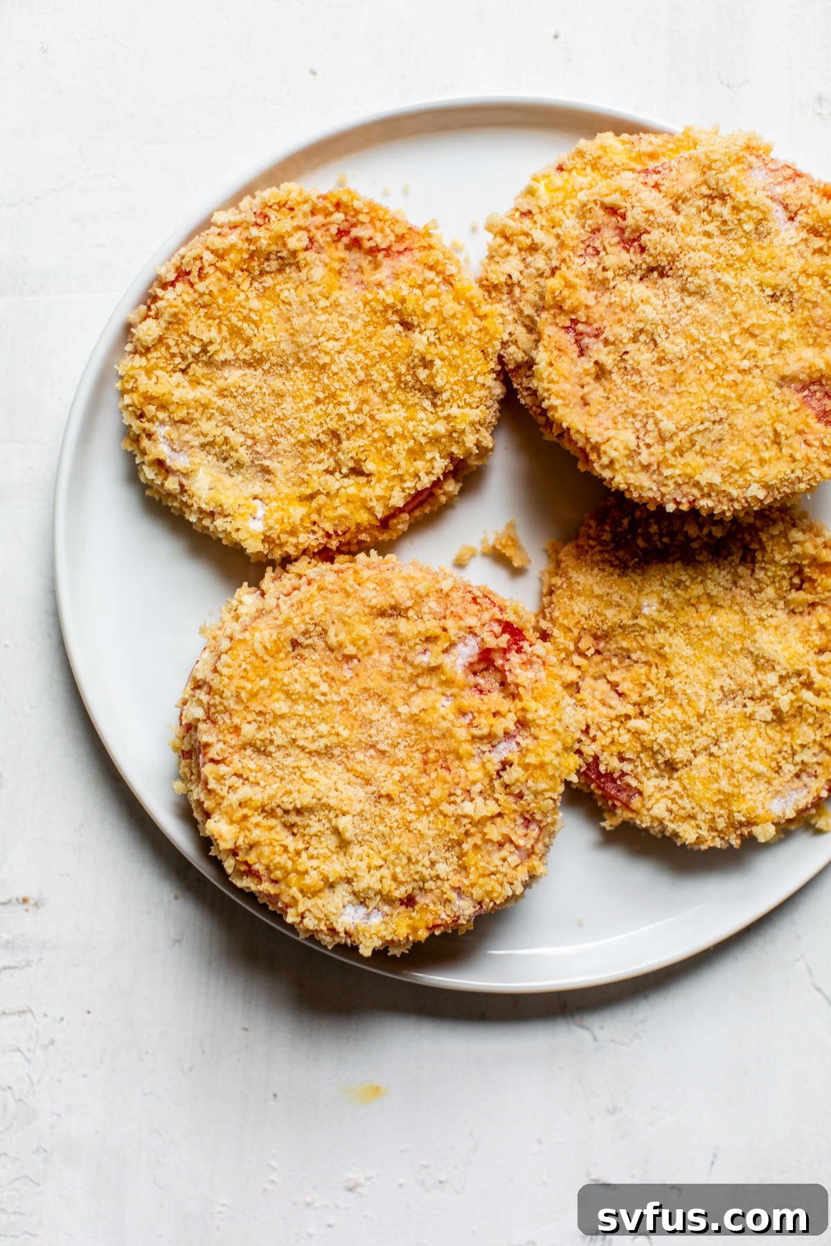 Tomato slices being coated in Panko breadcrumbs as part of the breading process, showing a uniform and complete covering.