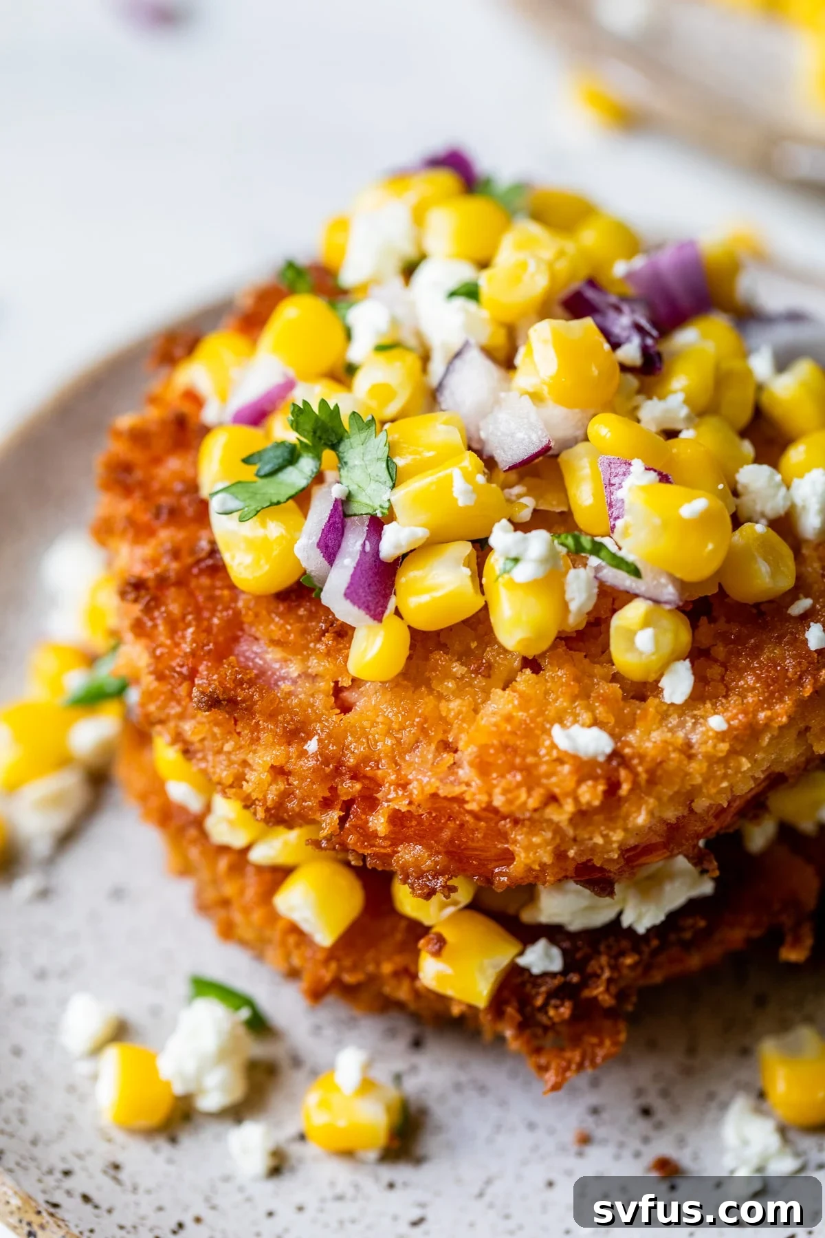 Close-up of crispy fried tomato slices stacked and generously topped with fresh corn salsa, garnished with cilantro.