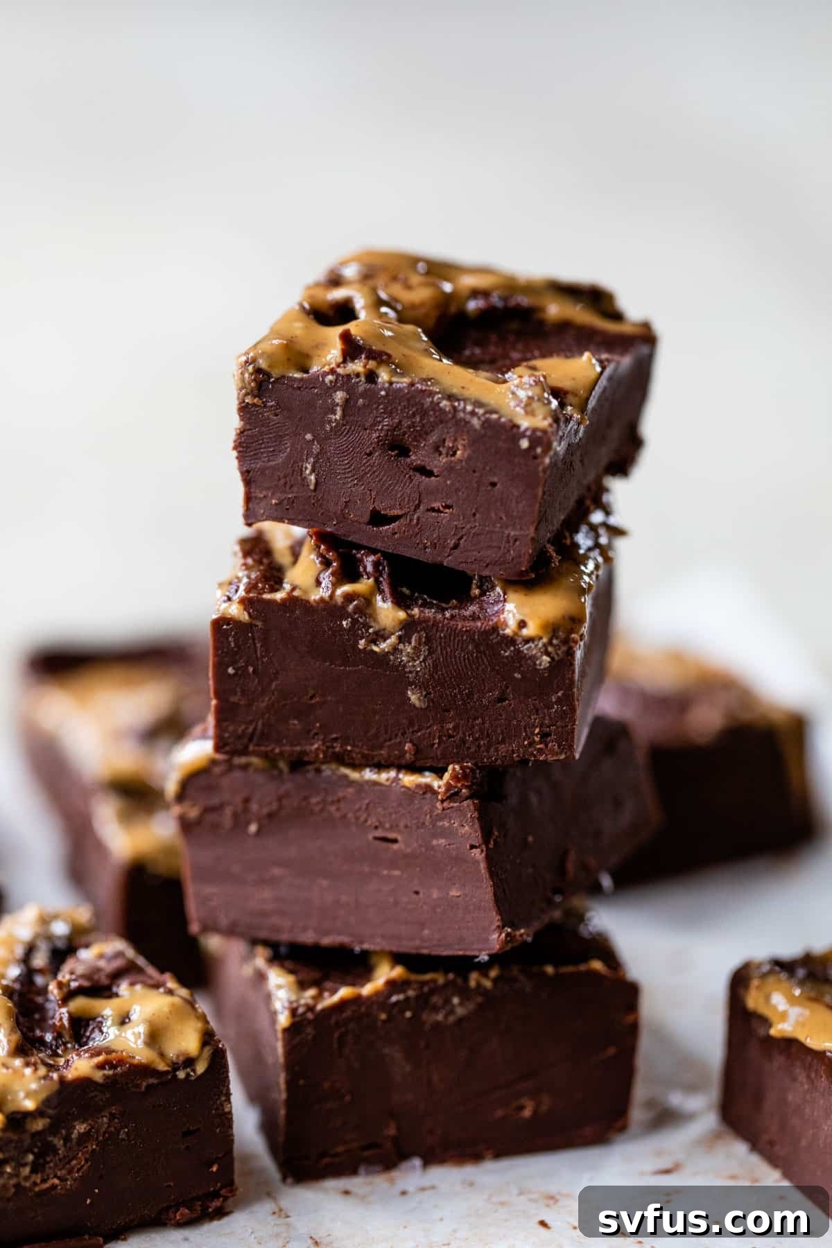 A stack of perfectly cut chocolate peanut butter fudge squares, beautifully drizzled with extra peanut butter.