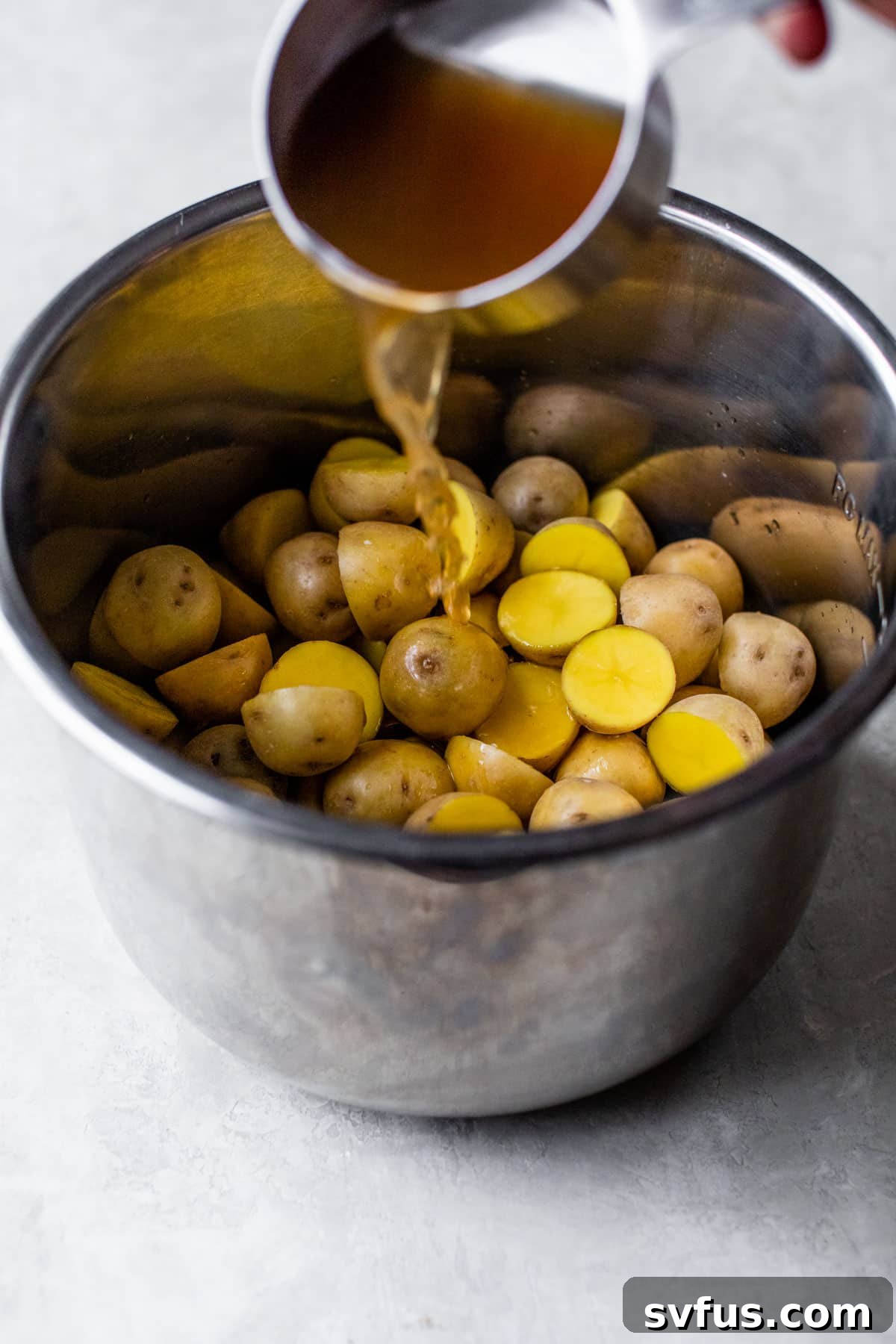 Vegetable broth being poured over baby potatoes and salt in an Instant Pot, prior to pressure cooking.