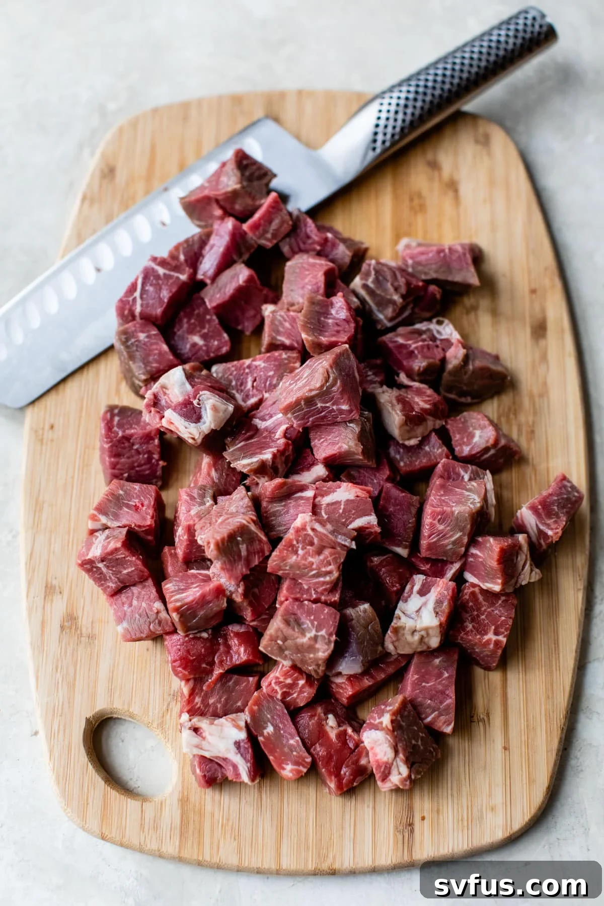 Raw steak bites on a cutting board next to a knife, ready for seasoning.