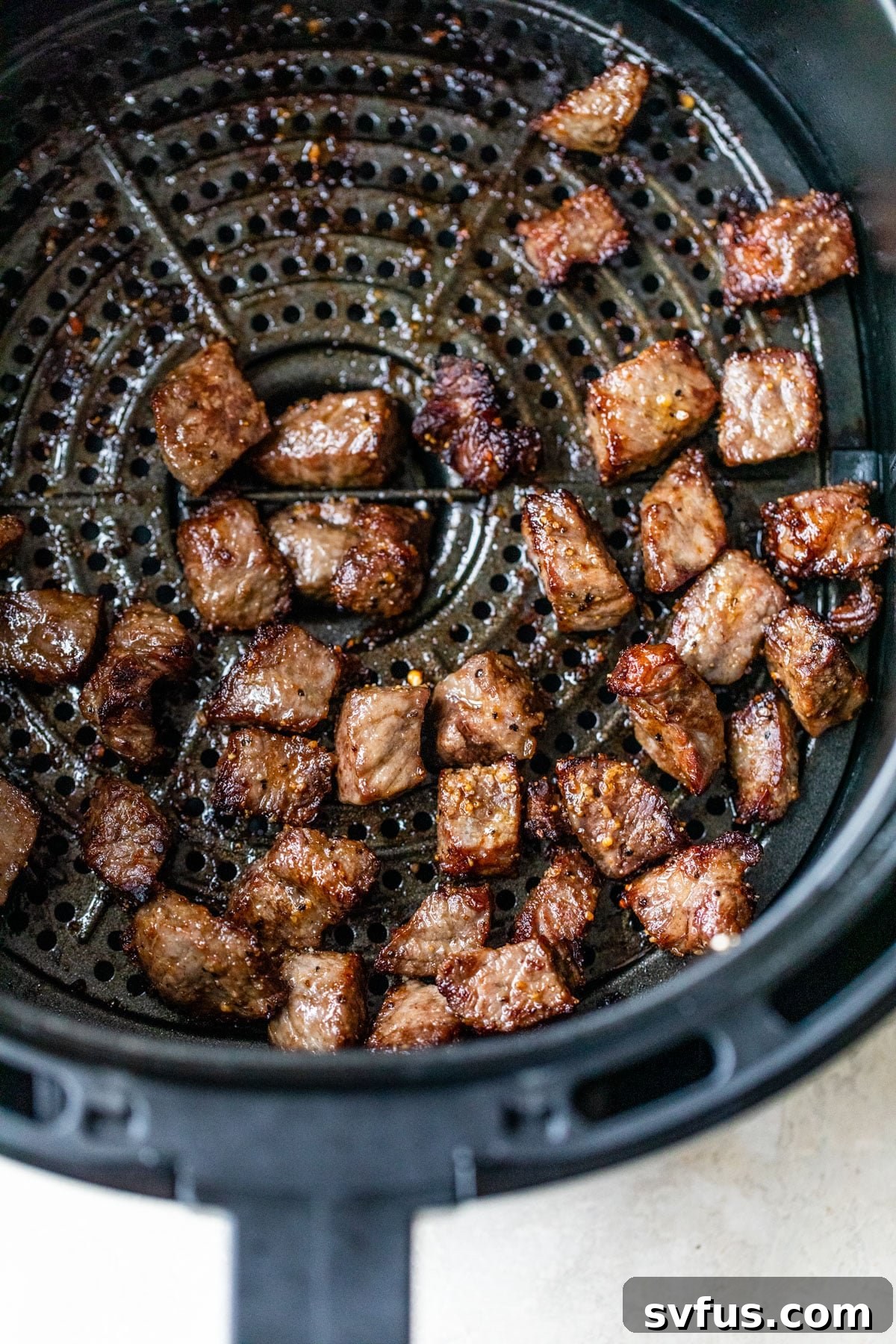 Steak bites cooking in a single layer inside an air fryer basket.