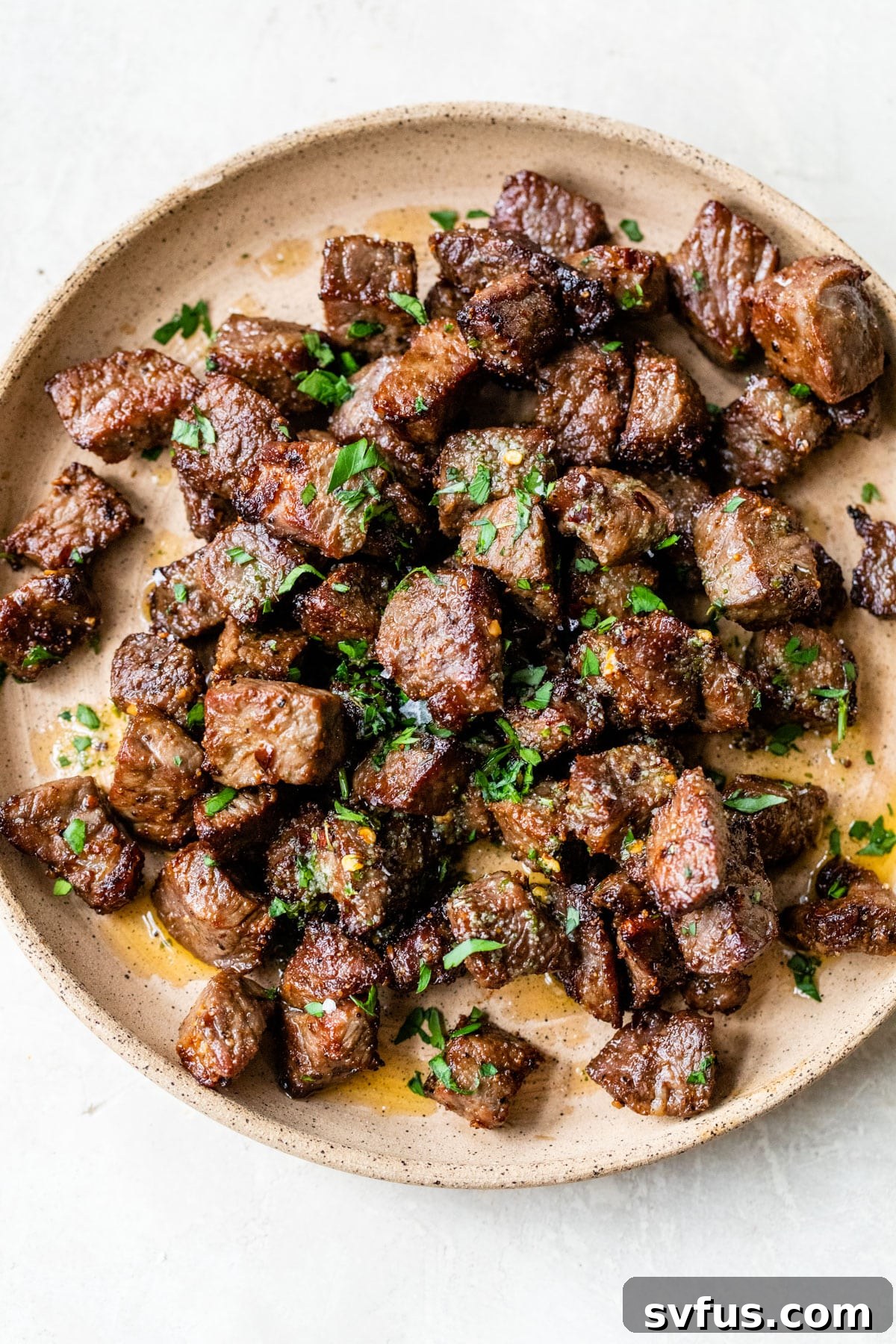 Perfectly cooked air fryer steak bites tossed in garlic butter, served on a plate.