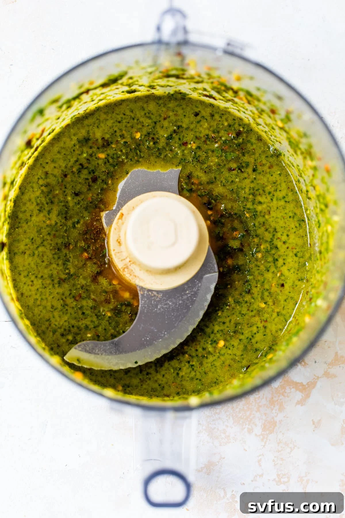 A food processor bowl filled with a vibrant green, herby chermoula sauce, indicating its fresh preparation.