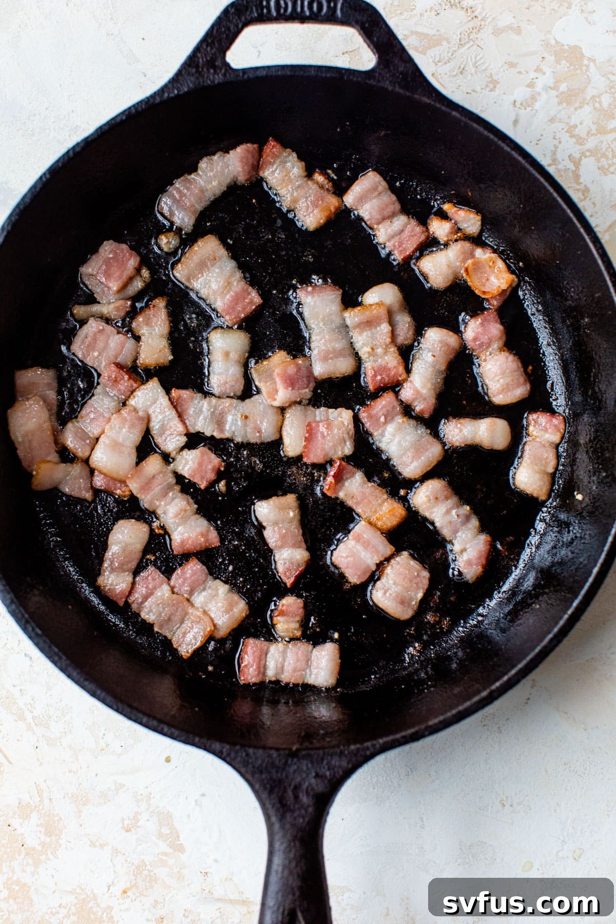 Chopped bacon sizzling in a cast iron skillet over medium heat.