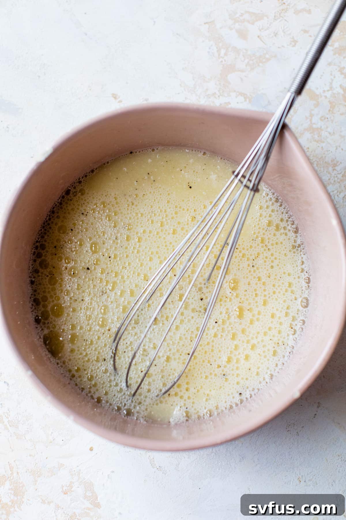 A bowl containing whisked egg whites, cottage cheese, and seasonings, ready for the frittata.
