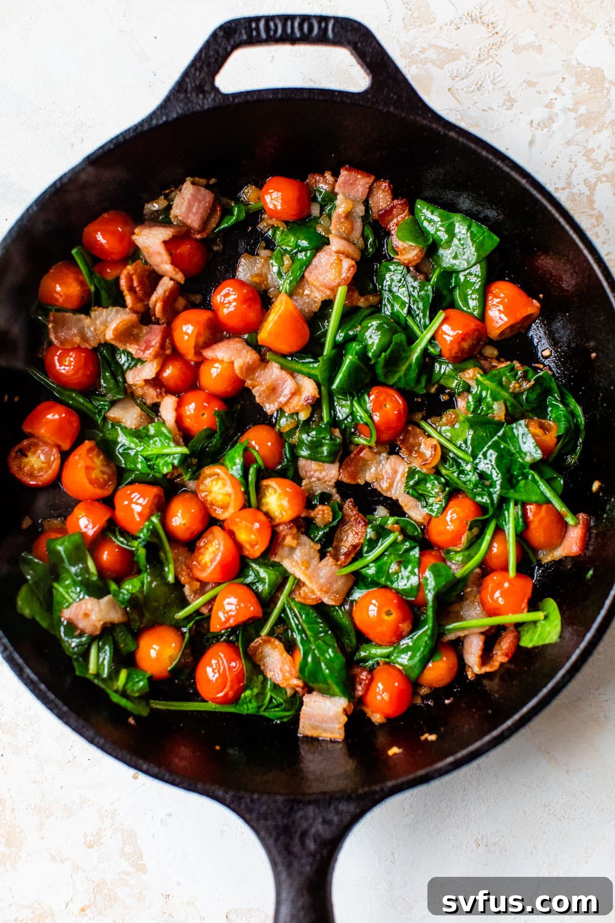 Sautéed bacon, shallots, and cherry tomatoes in a cast iron skillet, with spinach just added.