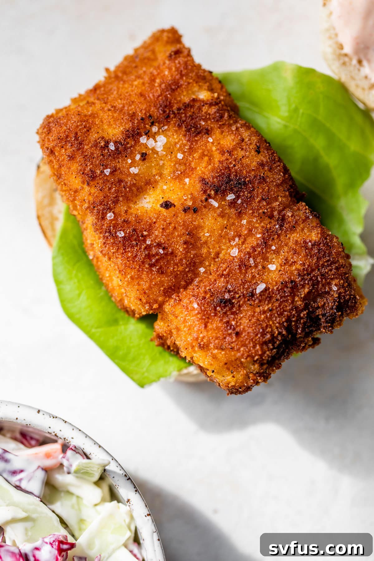 a piece of fried cod on a bottom burger bun with sauce