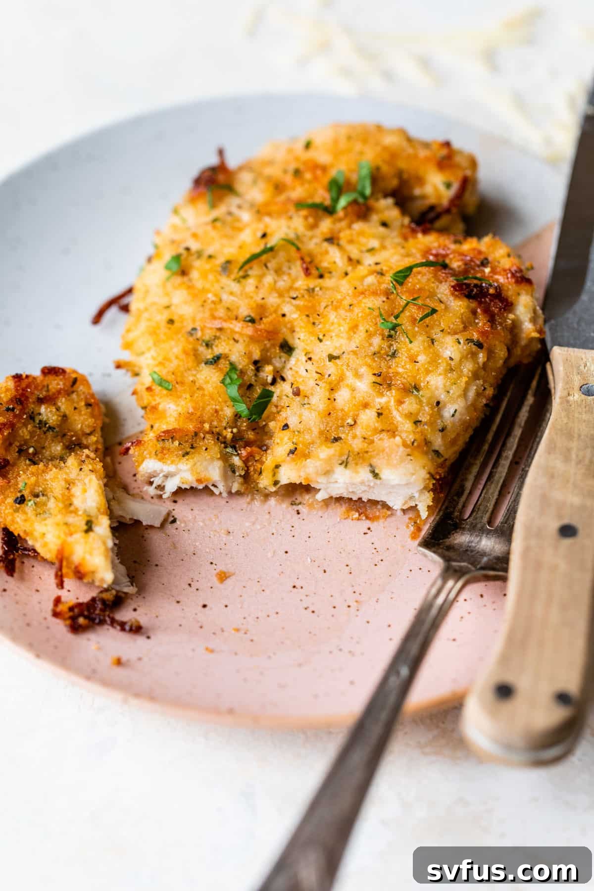 Baked Parmesan Chicken with a bite taken out, served on a plate with a fork, showing its golden, cheesy crust and tender interior.