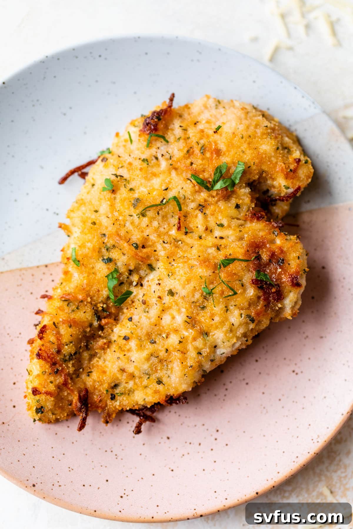 A perfectly baked parmesan chicken breast, golden and crispy, resting on a white plate, ready to be served.
