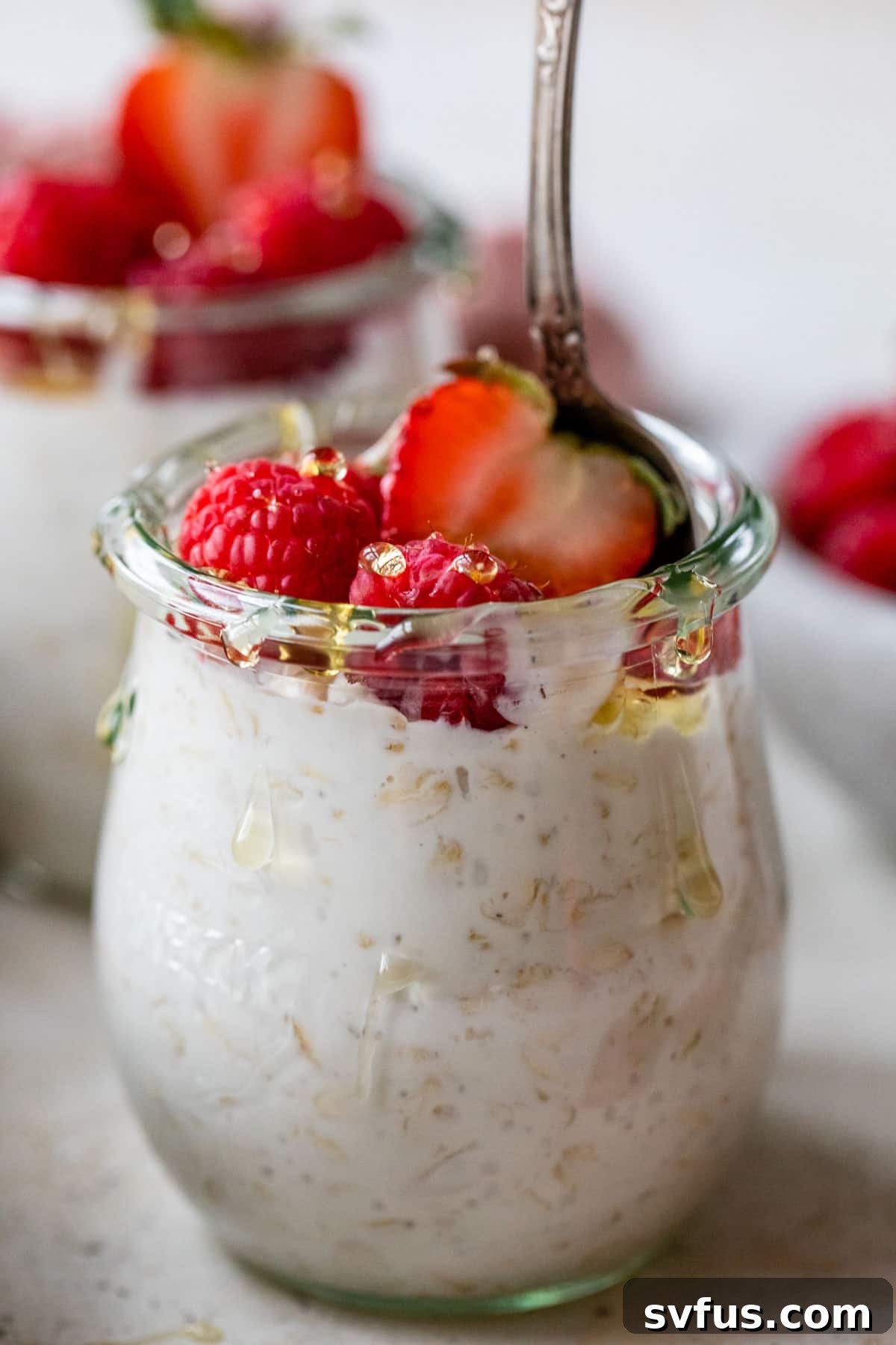 overnight oats in a mason jar with a spoon with raspberries and strawberries on top