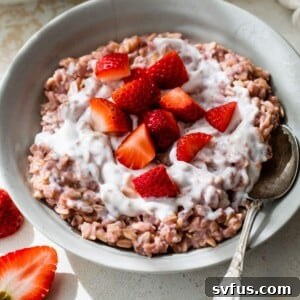 A bowl of vibrant pink strawberry oatmeal topped with creamy yogurt and fresh chopped strawberries.