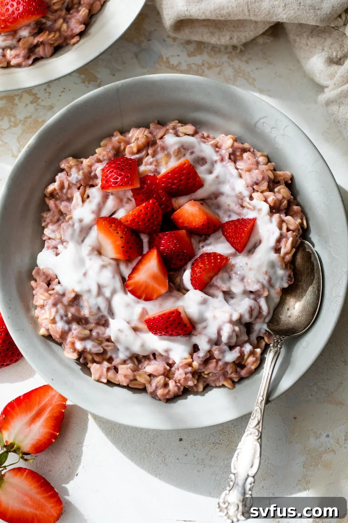 A beautifully presented bowl of creamy pink strawberry oatmeal with a spoon, generously topped with fresh yogurt and vibrant strawberry slices, inviting a delicious bite.