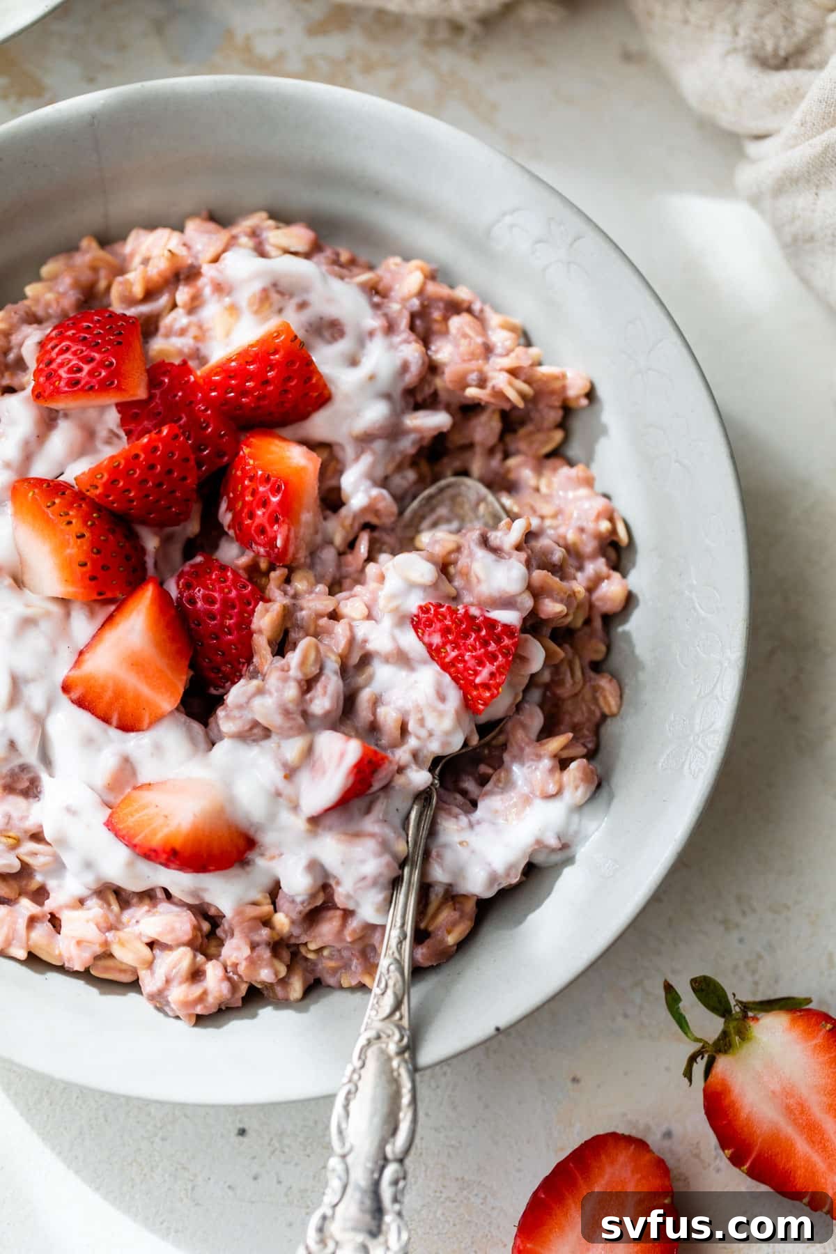 A close-up shot of a bowl of delicious pink strawberry oatmeal with a spoon, showing its creamy texture, as if someone is enjoying a bite.