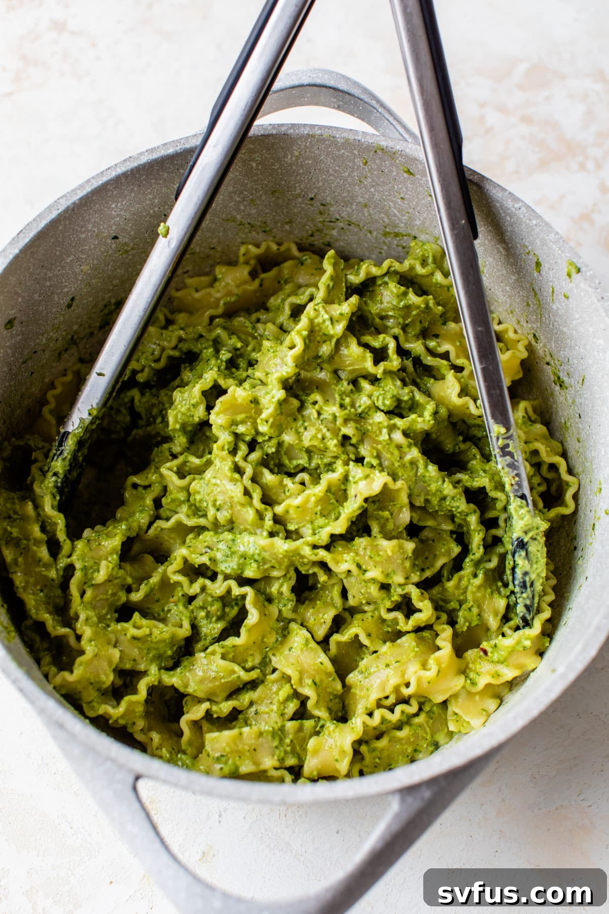 A large pot filled with creamy avocado pesto pasta, ready to be served, with serving tongs resting inside the pot.