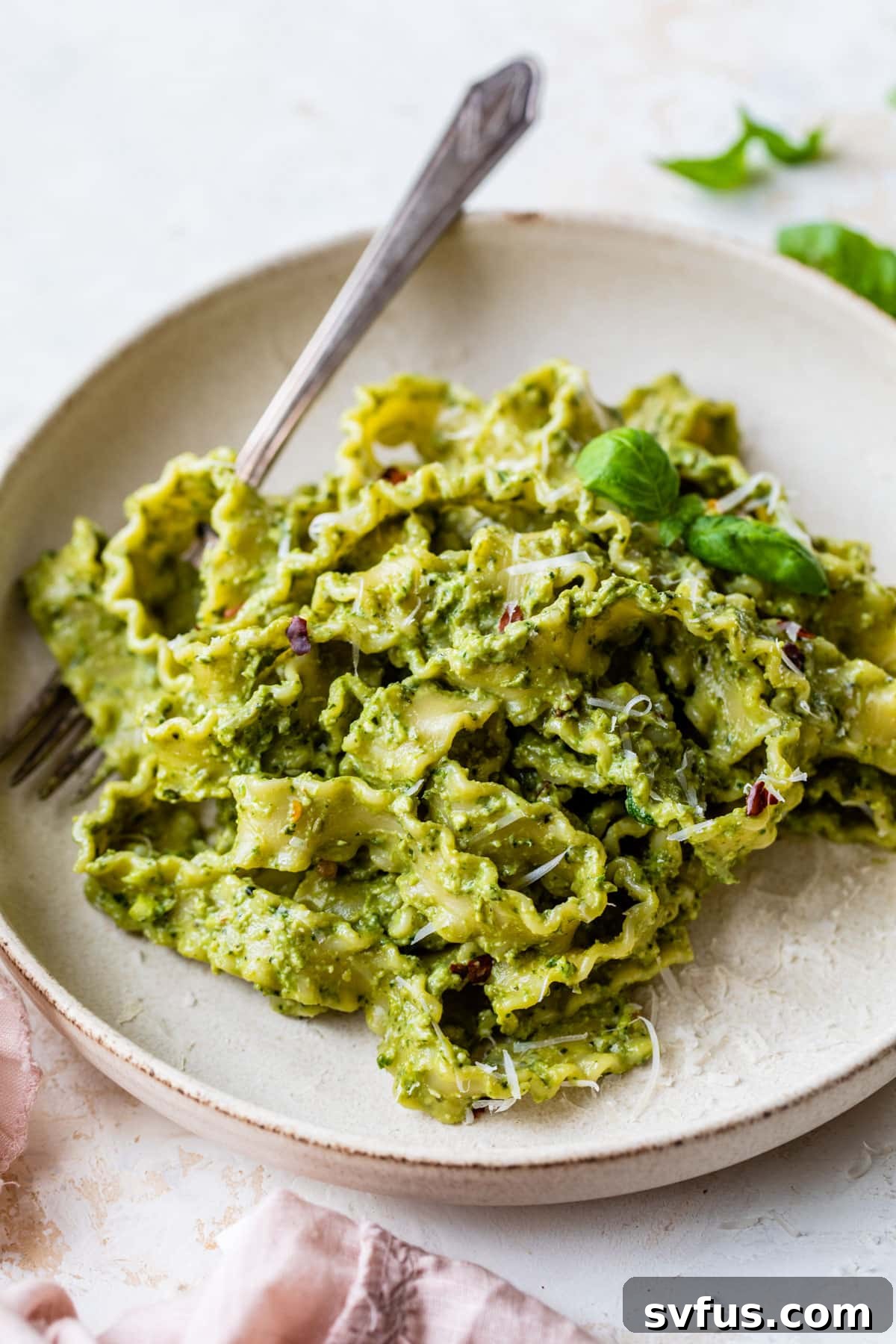 A beautifully plated dish of creamy avocado pesto pasta with a fork, garnished with fresh basil leaves, showcasing its vibrant green color and inviting texture.