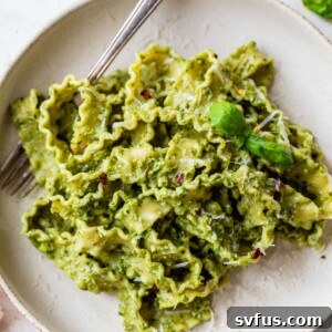 Avocado pesto pasta on a plate with a fork, garnished with fresh basil, ready to be eaten.