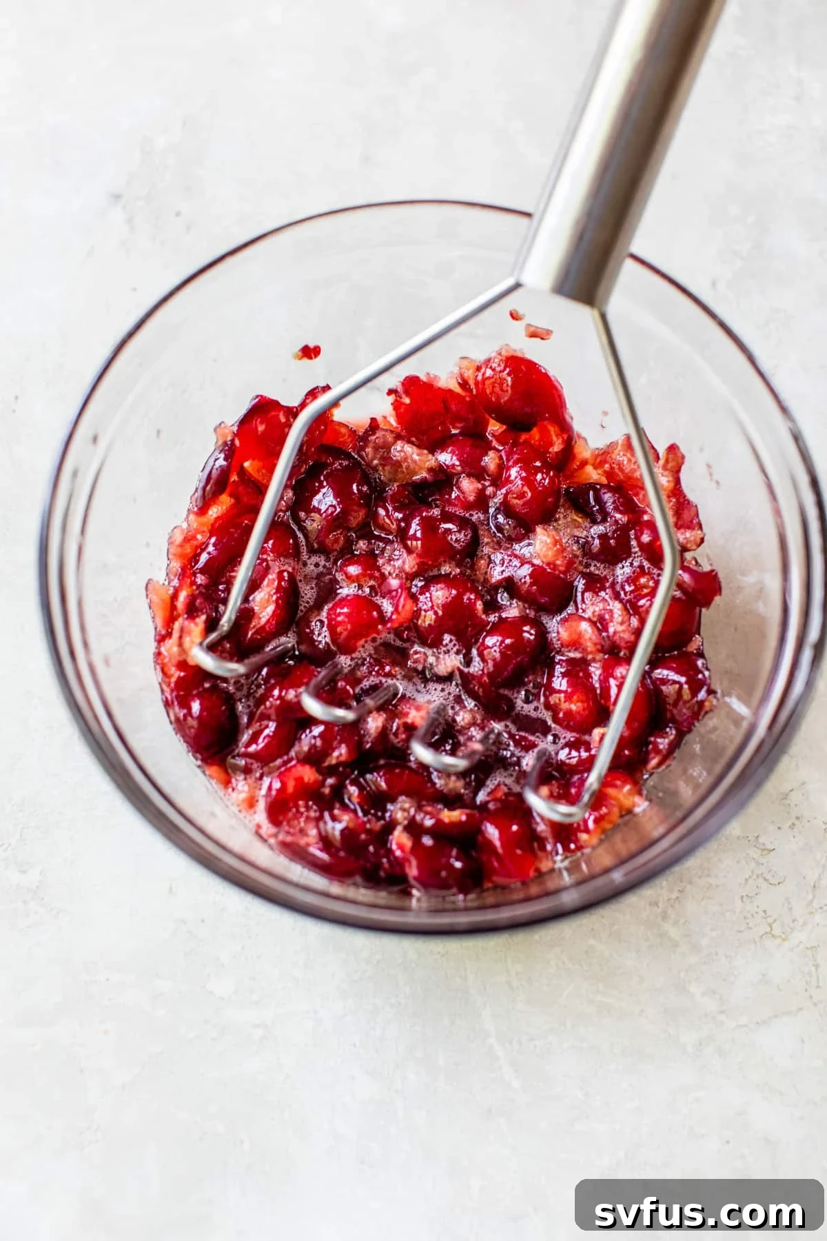 Freshly mashed pitted cherries in a glass bowl, prepared for the sweet and tangy crumb bar filling.