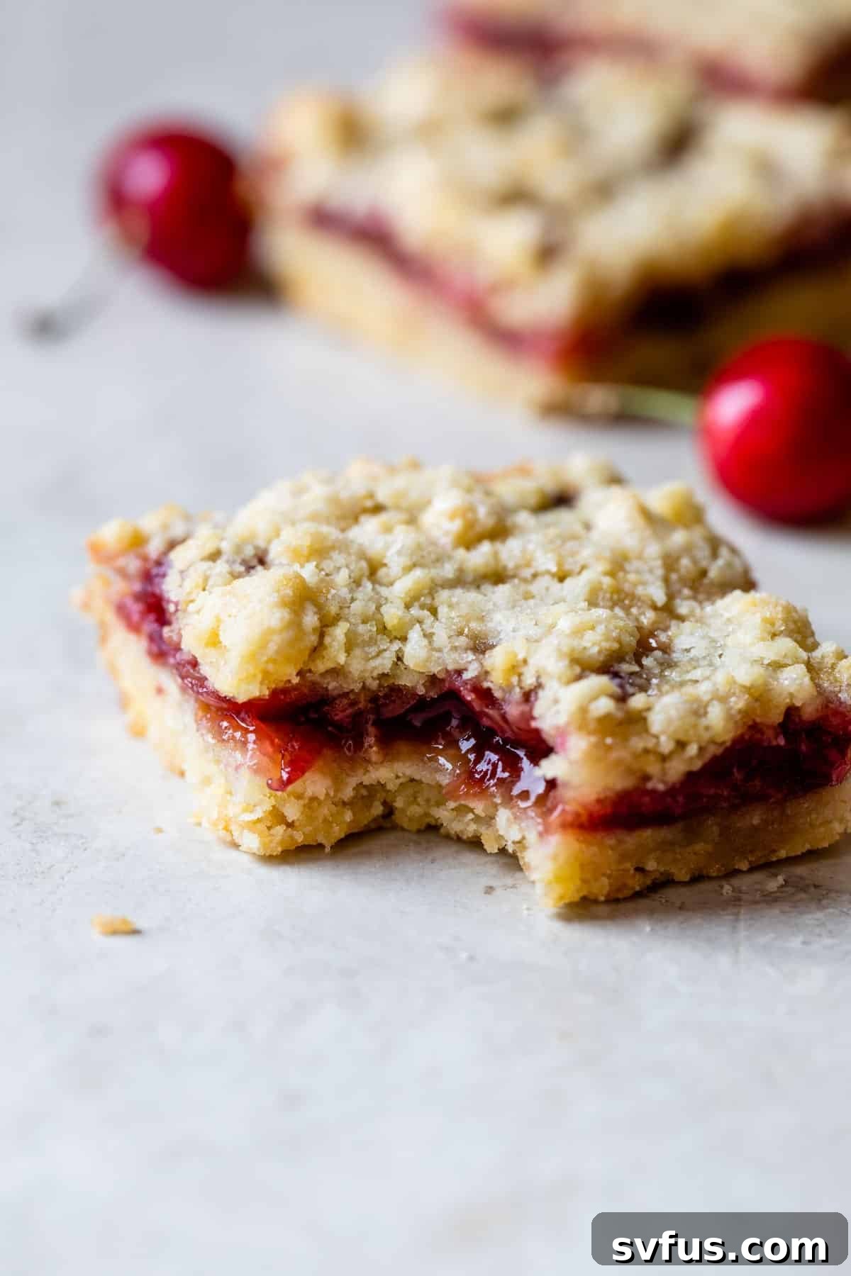 A single cherry crumb bar with a bite taken out, revealing the vibrant cherry filling and crumbly texture.