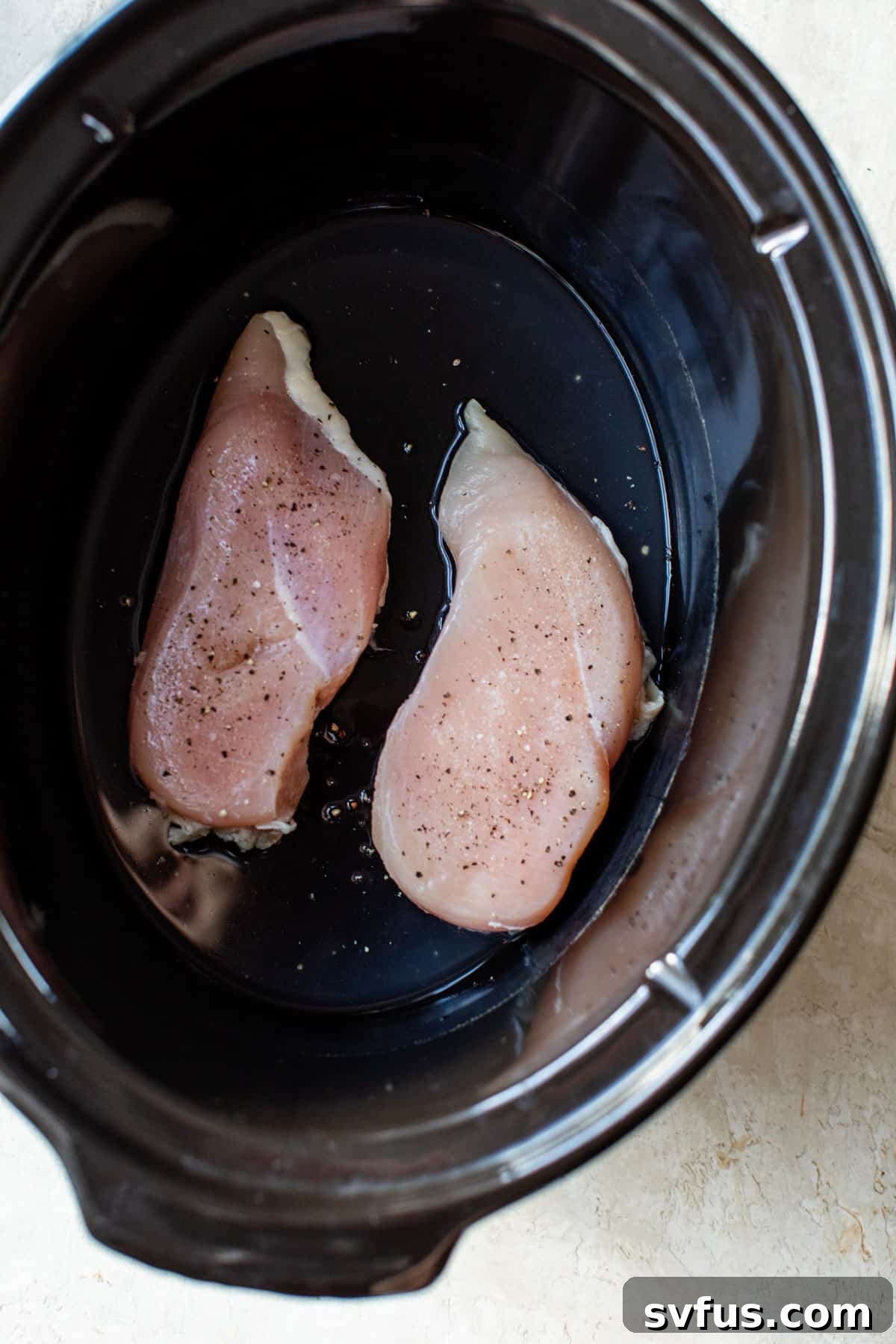 Two chicken breasts seasoned and placed inside a slow cooker.