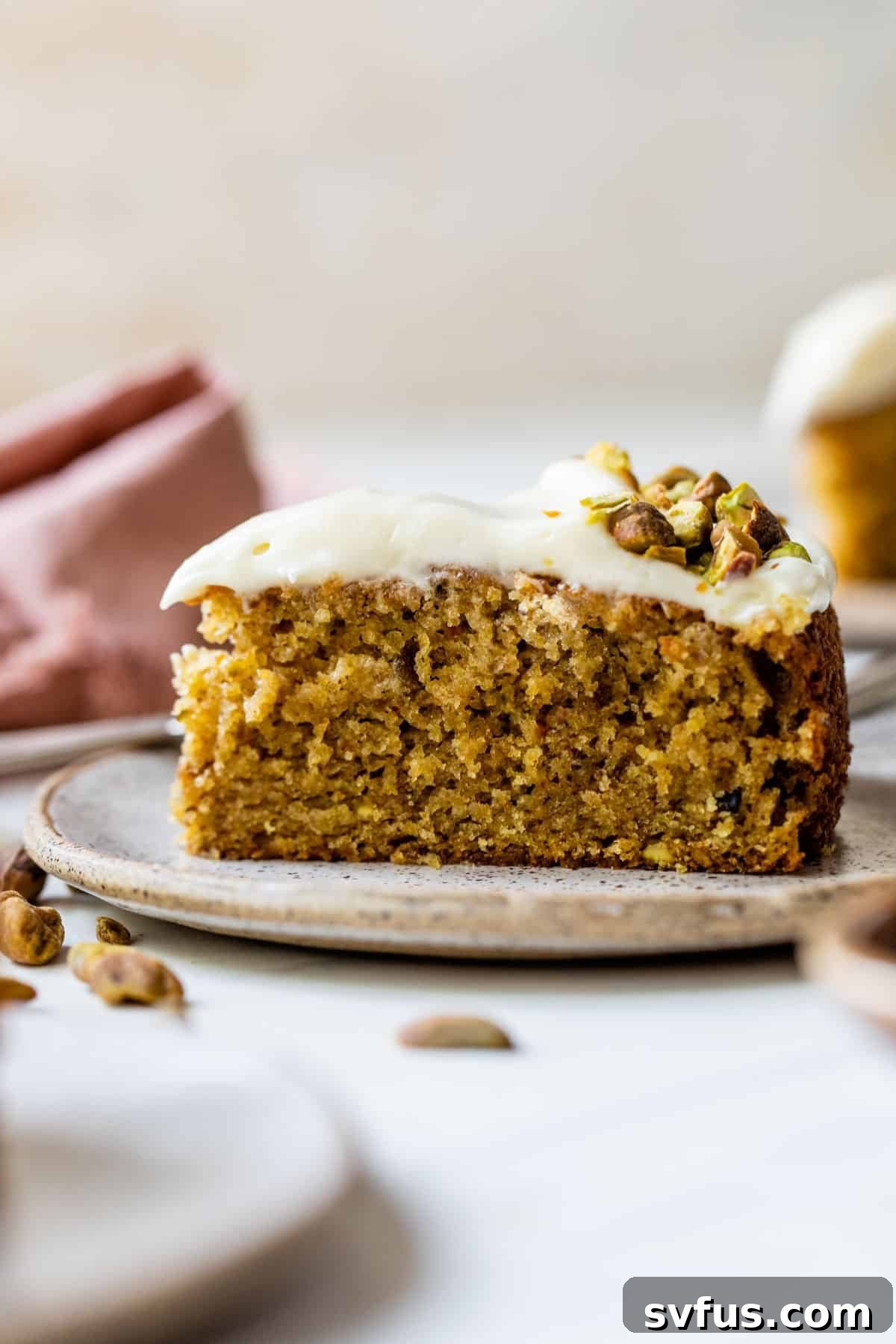 A beautifully sliced pistachio cake on a plate, adorned with creamy white frosting and chopped pistachios, showcasing its natural green hue.
