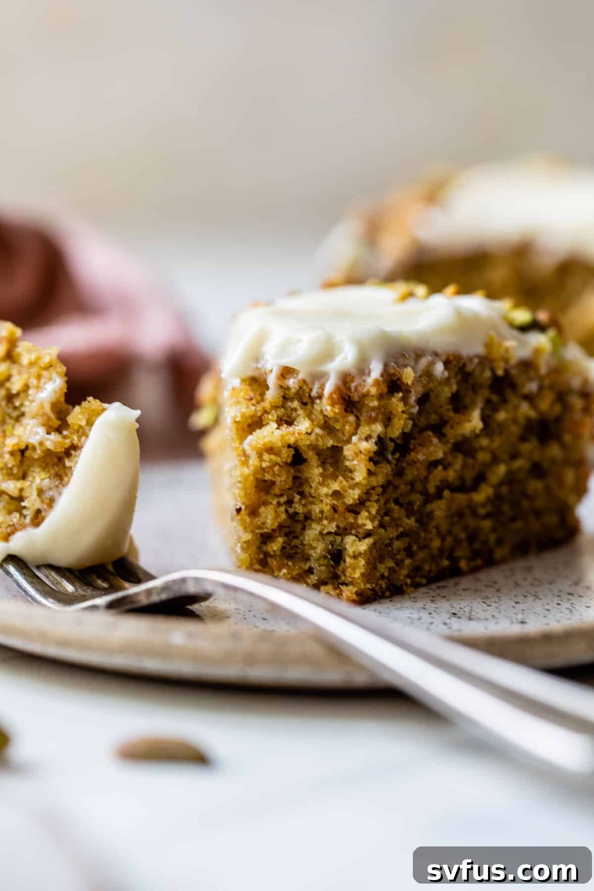 A close-up of a slice of pistachio cake on a white plate with a fork taking a bite, emphasizing its moist crumb, creamy frosting, and delightful texture.