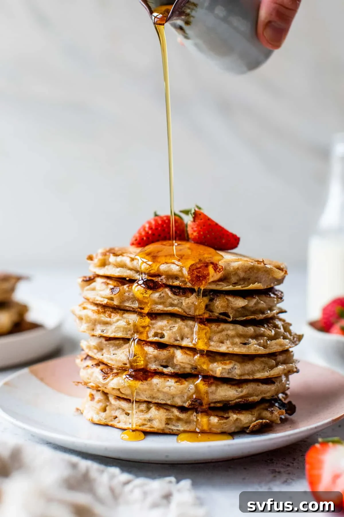 A beautifully stacked tower of golden cottage cheese pancakes, drizzled with maple syrup and garnished with fresh strawberries, viewed from the side.