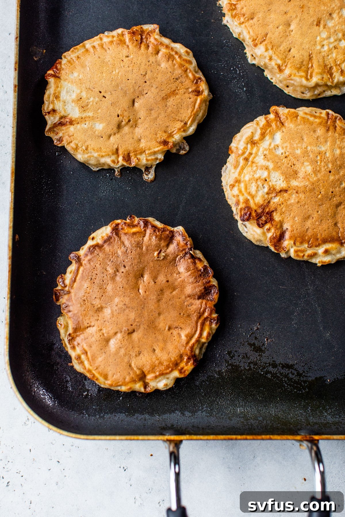 Several golden brown cottage cheese pancakes cooking on a griddle, with some already flipped and others showing bubbles on their surface, indicating readiness to flip.