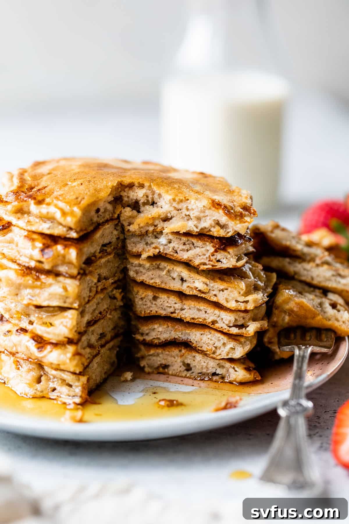 A side view of a stack of fluffy cottage cheese pancakes with a section already taken out by a fork, showcasing their soft and airy interior, drizzled with syrup.