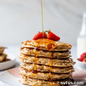 A stack of fluffy cottage cheese pancakes topped with strawberries and maple syrup.