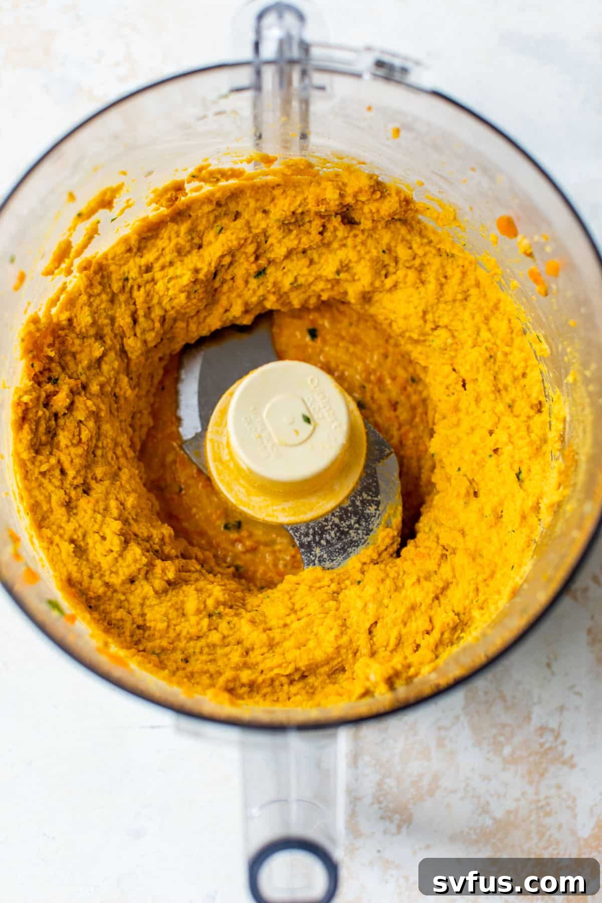 The blended carrot hummus ingredients swirling in a food processor, creating a smooth, orange mixture.