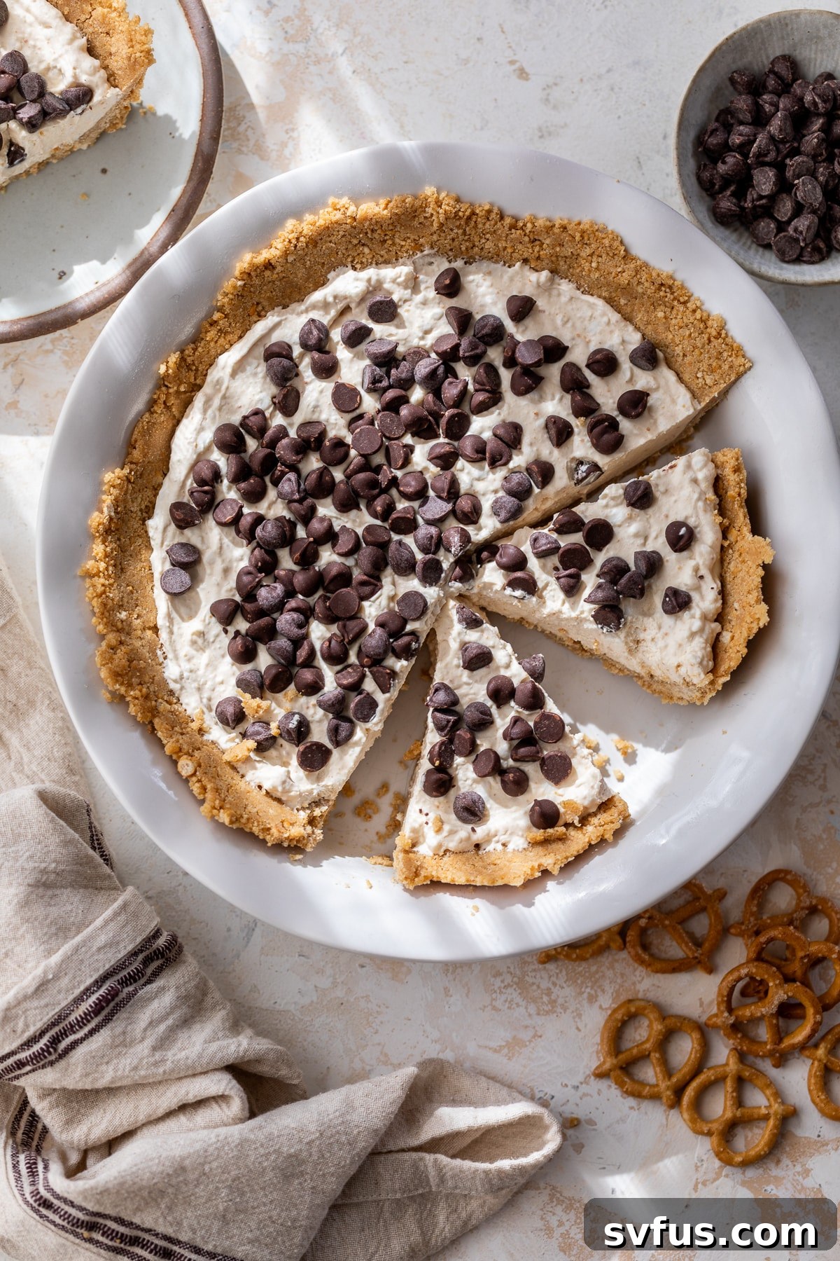 An overhead view of a whole peanut butter cottage cheese pie with several slices already cut and removed, showing the creamy filling and pretzel crust.